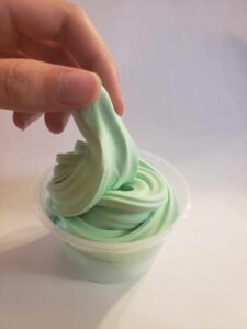 finger and thumb holding up a twist of green creamy slime